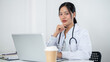 © bongkarn - A confident Asian female doctor smiling at the camera, sitting in front of her laptop at a desk.