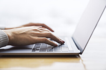 Wall Mural - Female hands typing on a trendy laptop keyboard, with a blurry office scene in the background