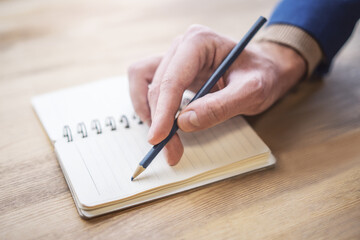 Poster - Sharp view of a man's hand transcribing in a notepad, with a defocused backdrop