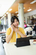 © Fahng - Young asian student talks on mobile while studying at canteen.