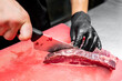 © pavel siamionov - A chef in black gloves slices fresh beef on a red cutting board. The focus is on the sharp knife and the marbled meat, highlighting culinary skills and food preparation.