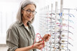 © Maria Vitkovska - Smiling, mature woman wearing stylish eyeglasses choosing new frame in optic store