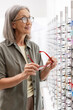 © Maria Vitkovska - Senior woman choosing eyeglasses in optical store: examining frames