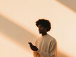 © aka_artiom - A young man sporting a trendy afro strikes a pose against a clean white backdrop while confidently holding his phone.
