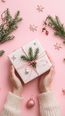 Wall Mural - female hands holding beautifully wrapped christmas present with pine branches and twine on pink back
