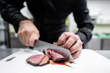 Canvas Print - A chef's hands skillfully slice a piece of juicy roast beef on a cutting board in a professional kitchen, showcasing culinary expertise and attention to detail.