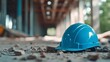 © Riko - A blue hard hat rests on a construction site floor among debris.