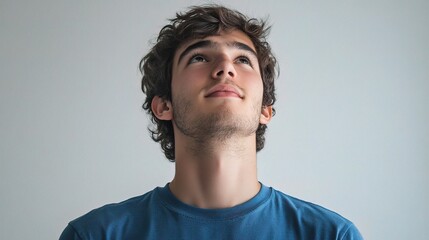 Wall Mural - Young Man Gazing Upward in Solid Blue Shirt Against Plain Background