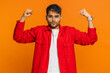 © Andrii Iemelianenko - I am strong and independent. Young Indian man showing biceps and looking confident, feeling power strength to fight for rights, energy to gain success win. Guy isolated on orange studio background