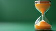 © Fotograf - An hourglass with orange sand on a green background, ideal for time-related and design concepts