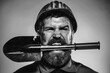 © Svitlana - Male builder or miner in protective helmet with shovel in teeth. Mining, heavy industry, construction concept. Portrait of angry bearded man in uniform and safety hard hat with spade. Black and white.