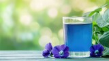Butterfly pea flowers and juice in a glass on a wooden table, green blurred light backdrop with ample room for adding text or branding