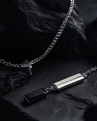 Poster - A sleek silver and black pendant necklace resting on textured dark rocks.