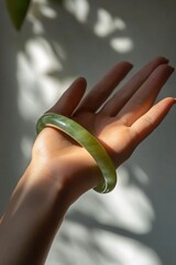 Poster - A hand holds a green jade bracelet, emphasizing its beauty and texture in soft lighting.