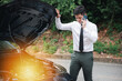 © sorapop - Worried driver calling roadside assistance for car engine failure. male businessman standing on highway, listening to operator with anxious expression. Concept for transportation problems and urgency