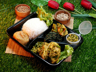 Wall Mural - Nasi Padang complete in black box is a traditional food from Padang. Indonesia. Decorated with cooking spices in a wooden bowl, red flowers, and synthetic grass. Suitable for cooking articles.