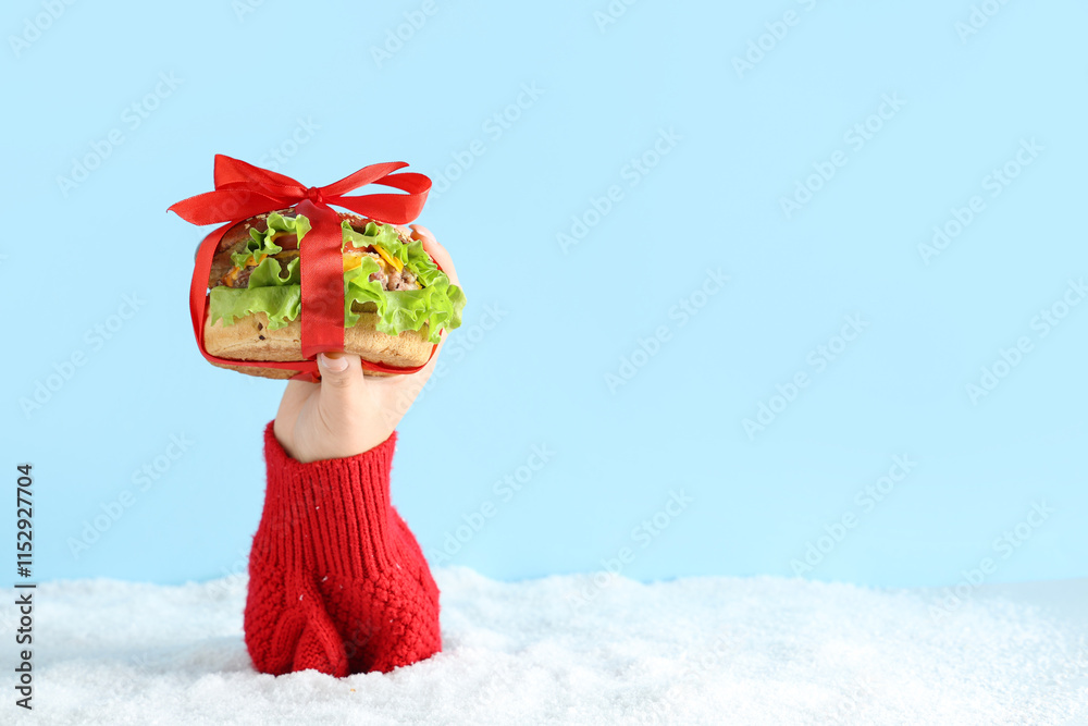 Female hand with tasty burger and snow on light blue background