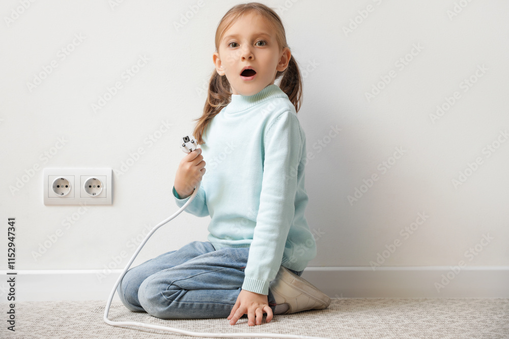 Shocked little girl with plug near socket at home. Child in danger