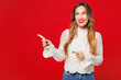 © ViDi Studio - Young smiling cheerful happy Caucasian woman she wears white blouse casual clothes point index finger aside on empty area mock up isolated on plain red background studio portrait. Lifestyle concept.
