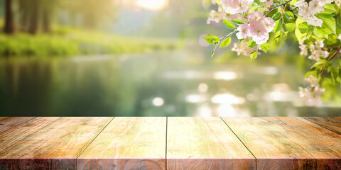 Poster - Spring nature background with green young foliage and flowering cherry branches with empty wooden decking in nature against lake.