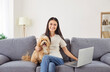 © Studio Romantic - Happy beautiful young woman with laptop computer and puppy dog at home smiling, relaxing in cozy modern living room interior, funny pet cuddling on sofa, spending weekend leisure, joyful fun moment