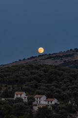 Wall Mural - Full moon rising over a hillside village at dusk.