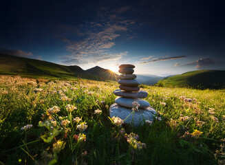 Poster - Serene sunset over a mountain meadow.  A carefully balanced stack of stones sits amidst wildflowers, conveying peace and balance.