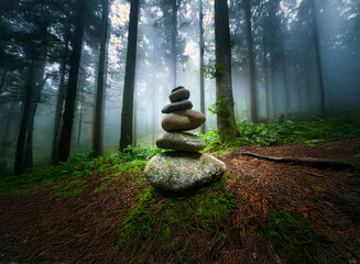 Poster - A serene stone cairn rests on moss in a mystical, fog-shrouded forest. Sunlight filters through the tall trees, creating a peaceful atmosphere.