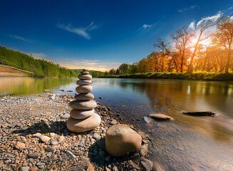 Aufkleber - Serene sunset scene: a carefully balanced stone cairn stands on a tranquil riverbank, reflecting the peaceful ambiance of nature.  The sun sets behind autumnal trees.