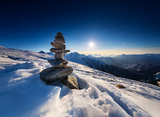 Poster - A serene winter mountain landscape. A carefully balanced stone cairn stands on a snow-covered peak, bathed in the golden light of the setting sun.  Vast, snow-covered mountains stretch to the horizon 