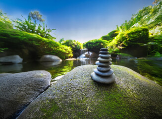 Poster - Serene garden scene with a stacked stone cairn by a tranquil pond and waterfall. Lush greenery and a clear blue sky create a peaceful atmosphere.  Zen garden, nature, balance.