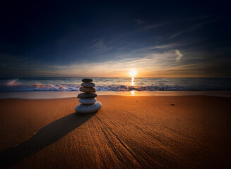 Poster - Serene sunset over ocean waves gently lapping a sandy shore.  A balanced stack of smooth stones sits peacefully, casting a long shadow.  Tranquil scene evokes calmness and mindfulness.