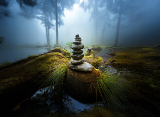Poster - Serene, misty forest scene. A carefully balanced rock cairn sits on moss-covered rocks near a still, dark pool.  Sunlight filters through the fog-laden trees.