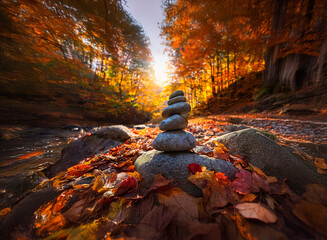 Poster - Serene autumn scene:  A balanced stack of grey stones rests on colorful fallen leaves beside a tranquil stream, bathed in the warm glow of the setting sun within a vibrant forest.