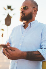 Fototapete - handsome bearded male holding smartphone using 4g connection in roaming for chatting, hipster guy wi