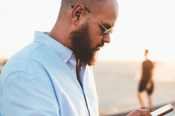 Fototapete - Pensive bearded guy installing application on smartphone via good internet connection on street, male hipster uploading content in social networks blogging via telephone cellular standing outdoors