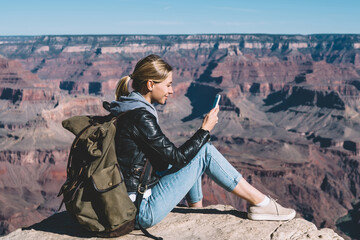 Wall Mural - smiling girl with rucksack using mobile connection for sending messages from rocky cliff in national