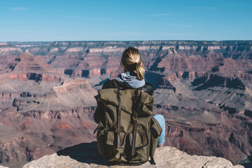 Wall Mural - back view of young woman with rucksack sitting on rocky cliff enjoying trip in usa exploring wild na