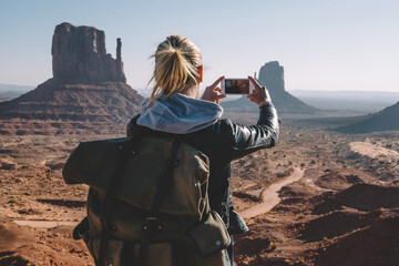 Wall Mural - back view of female with backpack photographing scenery landscape of monument valley using smartphon