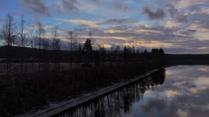 Wall Mural - car going on a road next to calm lake at sunset with a line of trees between the water and road