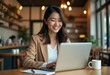 © Vibudhaart - A smiling woman working on her laptop in a coffee shop.