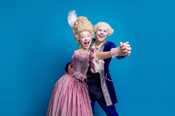 Wall Mural - A joyful couple dressed in vintage aristocratic costumes shares a dance against a vibrant blue background