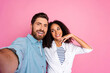© deagreez - Smiling young diverse couple taking selfie against a pink background in casual outfits
