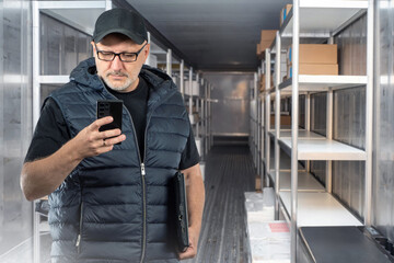 Poster - Man logistician. Driver with phone inside cargo van. Logistician writes SMS to supplier. Truck van with boxes on racks. Transport container with metal shelves. Man logistician from truck company