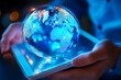 © MdArshed - Close up of human hands using tablet pc with glowing planet earth hologram