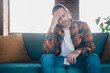 © deagreez - Young man with a stylish plaid shirt relaxing on a sofa, appearing thoughtful in a bright living room environment