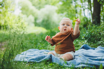 Wall Mural - Little boy 1 year old sitting on the grass in the park and eating bread. Baby on a walk in the fresh air.