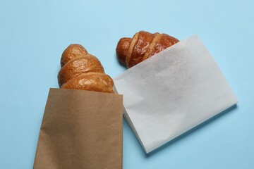 Wall Mural - paper bags with fresh croissants on light blue background, top view