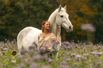 Wall Mural - A young woman cuddle and interact with her white spanish horese on a wildflower field in autumn outdoors