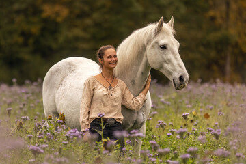 Wall Mural - A young woman cuddle and interact with her white spanish horese on a wildflower field in autumn outdoors